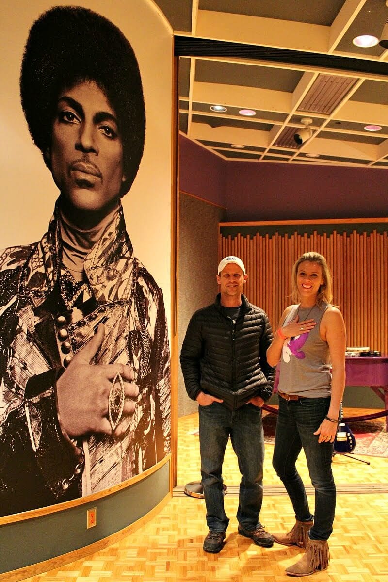 couple posing beside prince wall mural inside paisley park studio