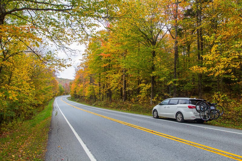 car on side of road next to new england fall foliage