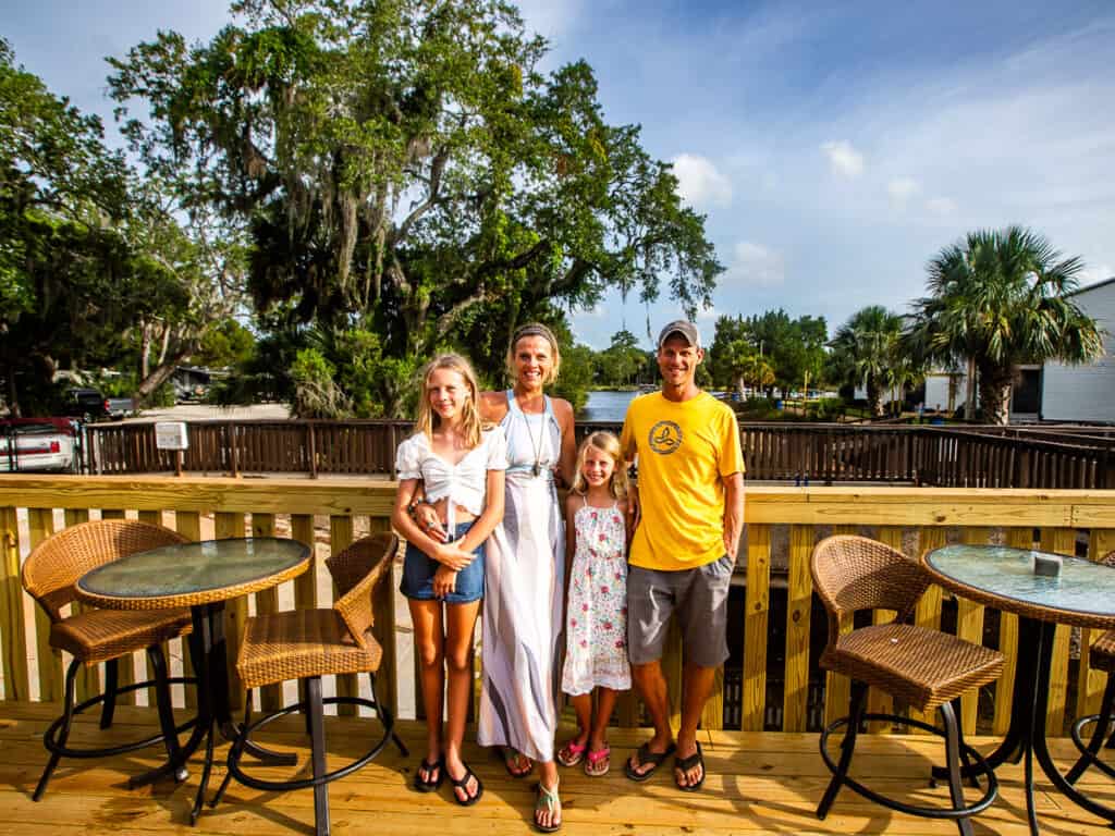 Family of four posing for a photo on a deck with a tree behind them.