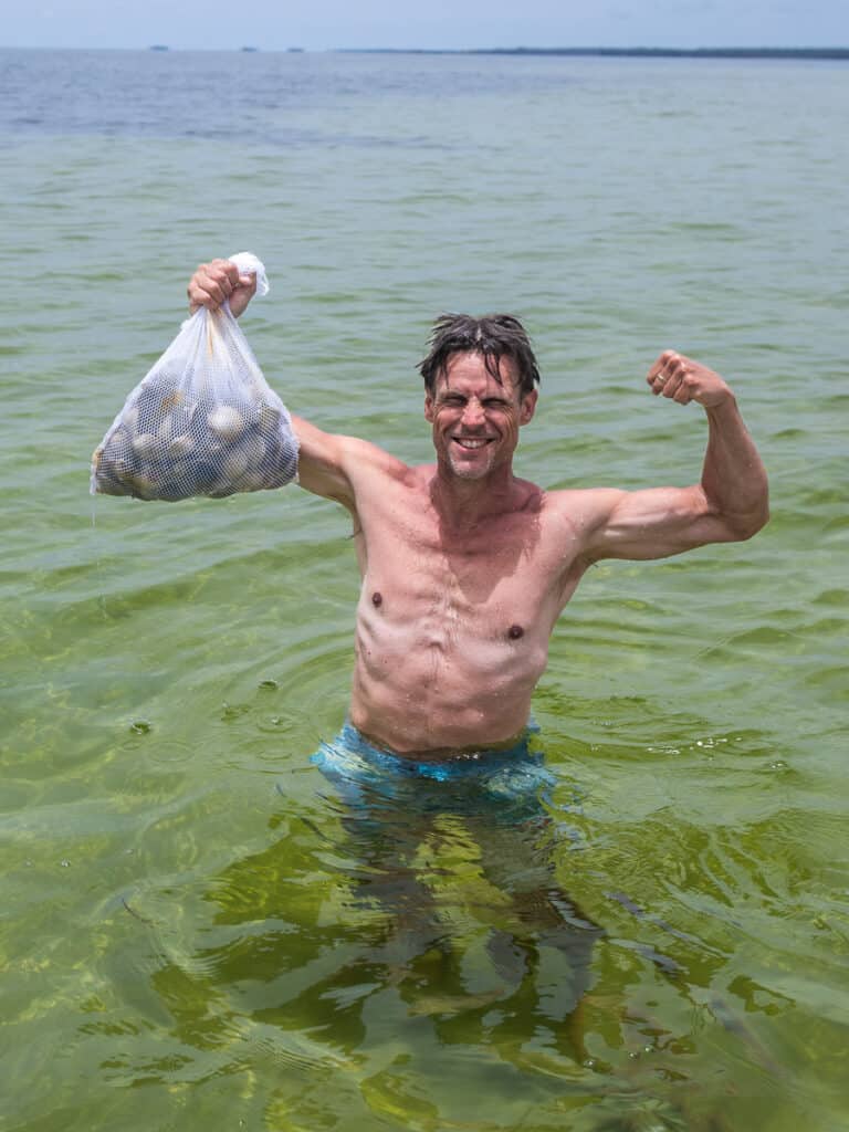 Man holding up a basket of clams standing in water.