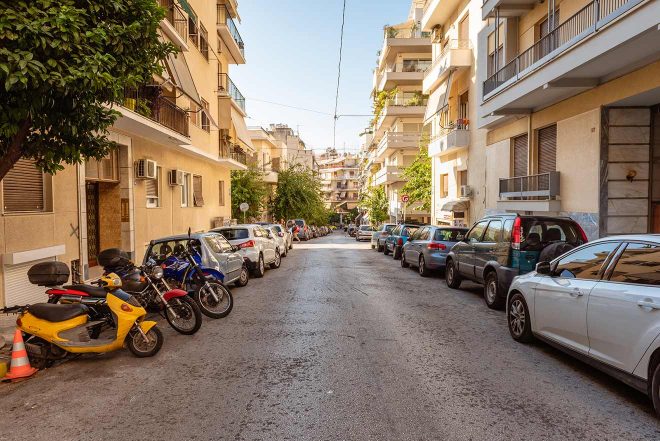 A typical Athenian street lined with parked cars and motorcycles, reflecting the everyday life and residential nature of the city.