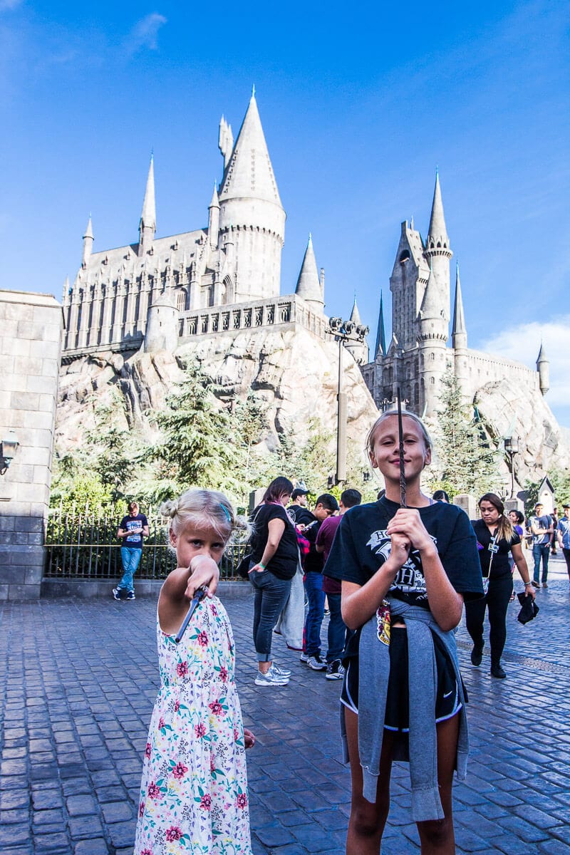 girls holding up wands in front of hogswart castle